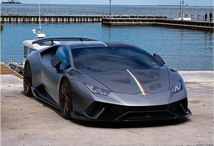 A grey lamborghini parked on the side of a body of water.