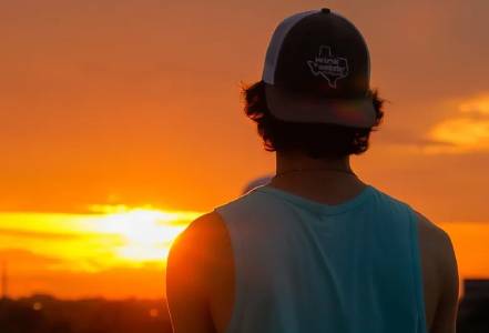 A man in a hat looking at the sun setting.